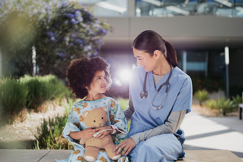 Medizinische Fachkraft mit Kind als Patient, das einen Teddybären hält.